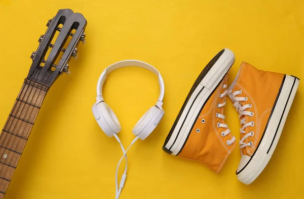 Creative layout. Acoustic guitar, Headphones and sneakers on yellow background. Top view. Flat lay