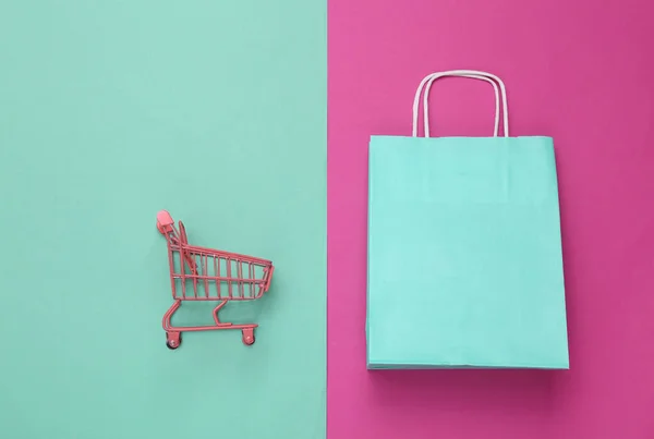 粉色蓝色背景的迷你购物车和纸制购物车 顶部视图 最低限度主义 — 图库照片