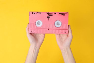 Sarı zemin üzerinde retro video kaseti tutan eller