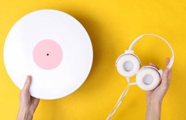 Beyaz kulaklık tutan kadın eller ve sarı arka planda plaklar. DJ, müzik konsepti