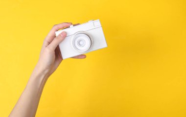 Eller sarı arka planda beyaz kamerayı tutuyor. Minimalizm
