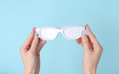 Mavi arka planda beyaz güneş gözlüğü tutan eller. Minimalizm