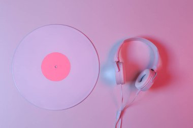 Pembe-mavi neon ışıklı kulaklıklı beyaz vinil plak. Minimalizm müzik konsepti. Üst görünüm