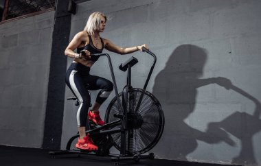 Egzersiz bisikleti üzerinde yoğun kardiyo eğitimi alan bir kadın. Spor salonunda jimnastik yapmak için hava bisikleti kullanan bir kadın.