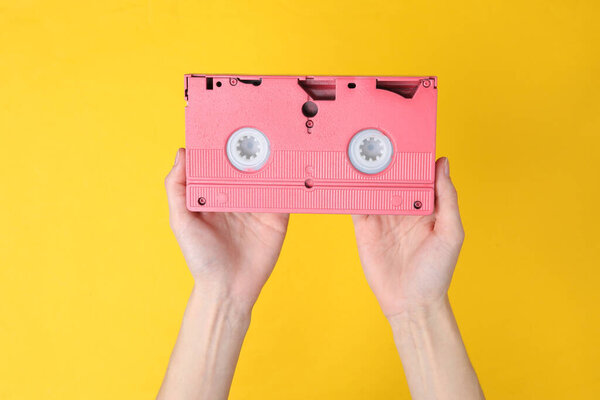 Hands holding retro video cassette on yellow background