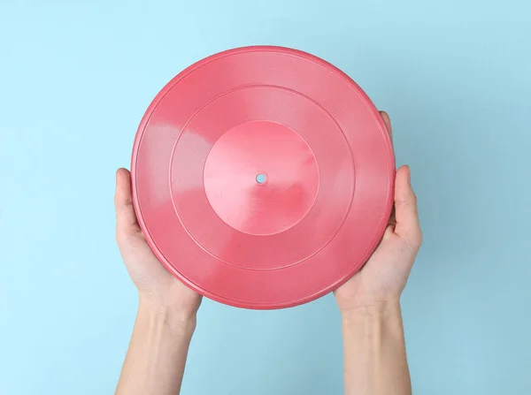 Female hands holding pink vinyl record on blue background. DJ, music concept