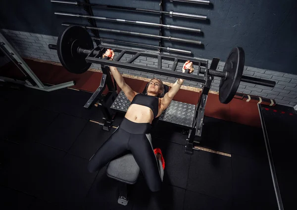 Fit woman lies on a bench and doing barbell press in a modern gym