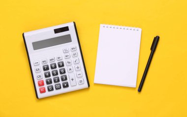 Sarı arka planda hesap makinesi ve defter. Üst Manzara. Düz yatıyordu