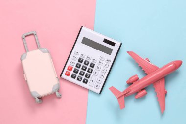 Seyahat konsepti. Mavi-pembe arka planda hesap makinesi, uçak ve bagaj. Üst Manzara. Düz yatıyordu