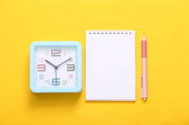 Sarı arka planda çalar saat ve defter. Üst görünüm