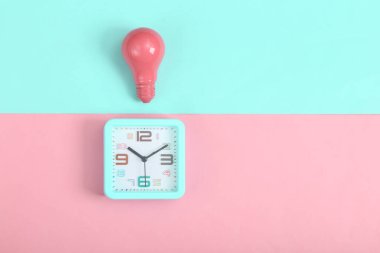 Pembe arka planda çalar saat ve pembe ampul. Minimalizm. Üst görünüm