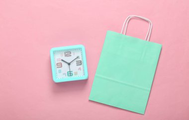 Alışveriş zamanı. Pembe arka planda çalar saat ve alışveriş paketi