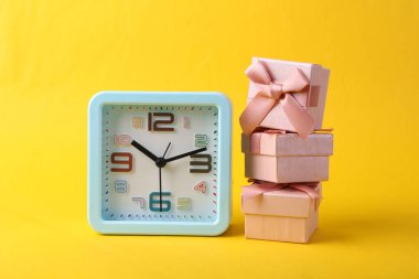 Sarı arkaplanda çalar saat ve hediye kutuları.