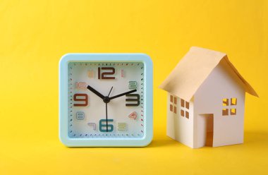 Sarı arkaplanda alarm ve ev figürü