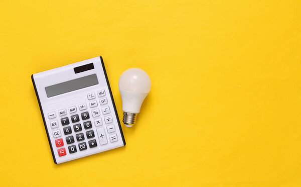 Calculator and led light bulb on yellow background. Top view. Flat lay. Copy space