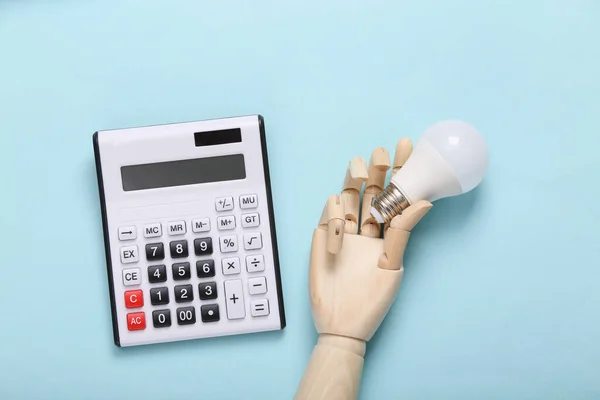 Mano Madera Sostiene Bombilla Calculadora Sobre Fondo Azul Vista Superior — Foto de Stock