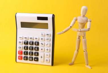 Tahta kukla sarı arkaplandaki hesap makinesini gösteriyor