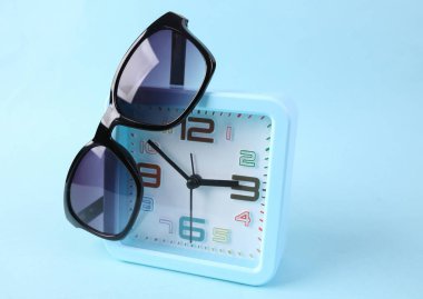 Mavi arka planda güneş gözlüklü çalar saat. Yaz zamanı.