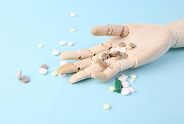 Mavi arka planda tahta bir el içinde haplar. Aşırı doz.