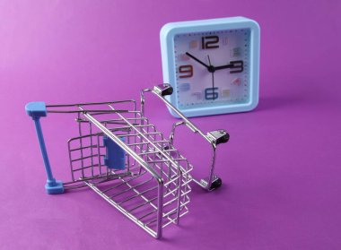 Mor arka planda alışveriş arabası olan bir saat. Alışveriş zamanı.