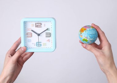 Beyaz arkaplanda çalar saati ve küreyi tutan eller