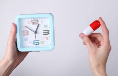 Beyaz arka planda çalar saat ve hap tutan eller