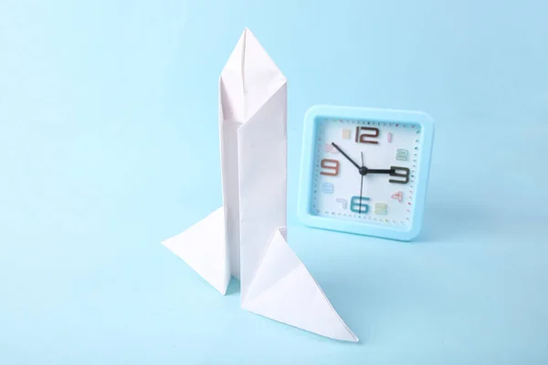 Startup. Paper rocket and alarm clock on blue background