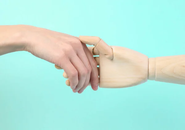 Human and wooden hand puppets shake hands on blue background