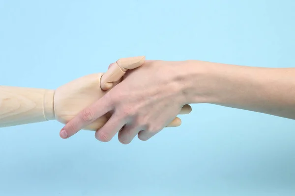 Human and wooden hand puppets shake hands on blue background