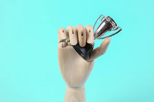 Wooden hand holds winner cup on blue background.
