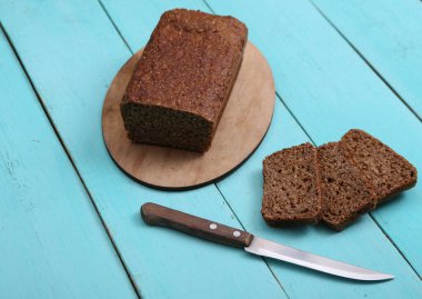 Mavi ahşap arka planda bıçaklı tam tahıllı çavdar ekmeği.