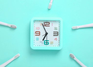 Mavi arka planda çalar saati olan plastik diş fırçaları. Diş bakımı konsepti. Üst görünüm