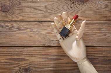 Tahta el, ahşap arka planda kırmızı ruj tutar.