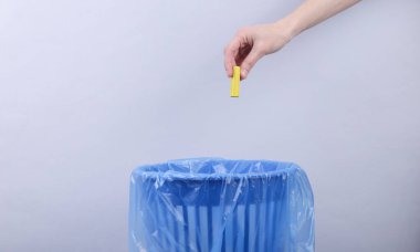 El, gri arka planda paketli çöp kutusuna pil atıyor.