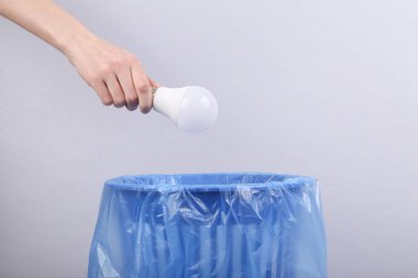 El, gri arka planda paketli çöp kutusuna ampul atıyor.