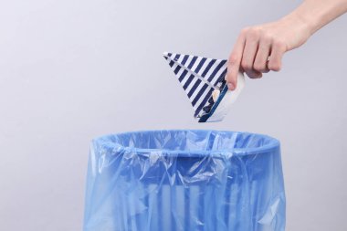 El, oyuncak yelkenliyi gri arka planda paketi olan çöp kutusuna atar.