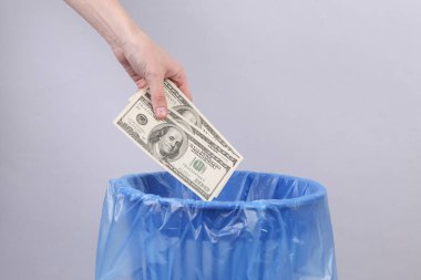 El, dolar banknotlarını gri arka planda paketli çöp kutusuna atıyor.