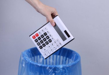 El, gri arka planda paketi olan hesap makinesini çöp kutusuna atar