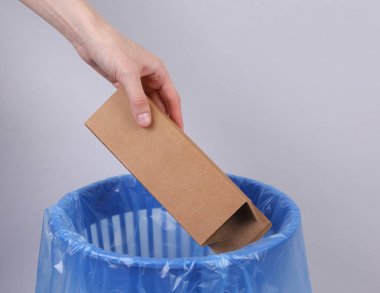 El, gri arka planda paket olan karton kutuyu çöp kutusuna atar.