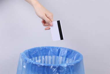 El, kredi kartını gri arka planda paketli çöp kutusuna atıyor.