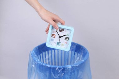 El, gri arka planda paketli çöp kutusuna çalar saat atar