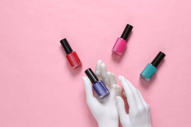 Beyaz manken elleri pembe arka planda oje şişeleri tutuyor.