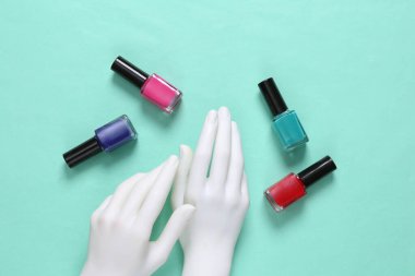 Beyaz manken elleri ve mavi arka planda oje şişeleri.