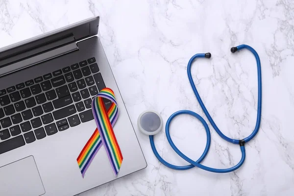LGBT rainbow ribbon pride tape symbol and stethoscope, laptop on marble background. Top view