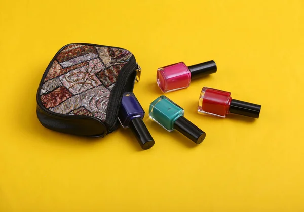 Cosmetic bag with bottles of nail polish on yellow background