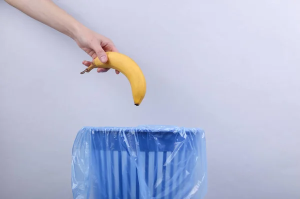 Рука Бросает Банан Мусорный Бак Пакетом Сером Фоне — стоковое фото
