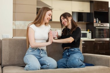 Çak bakalım. Oturma odasındaki kanepede oturmuş çay içen iki mutlu kız arkadaş.