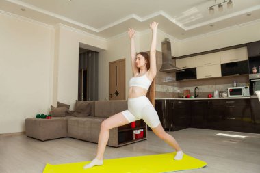 Genç bir kadın oturma odasında yoga yapıyor. Spor haberleri.