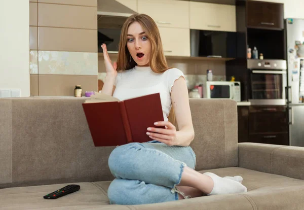 Emocionální Překvapení Mladá Žena Čtení Knihy Zatímco Sedí Pohovce Obývacím — Stock fotografie