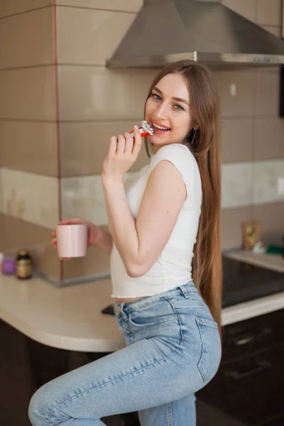 Νεαρή Χαρούμενη Γυναίκα Πίνει Καφέ Και Τρώει Σοκολάτα Στην Κουζίνα — Φωτογραφία Αρχείου
